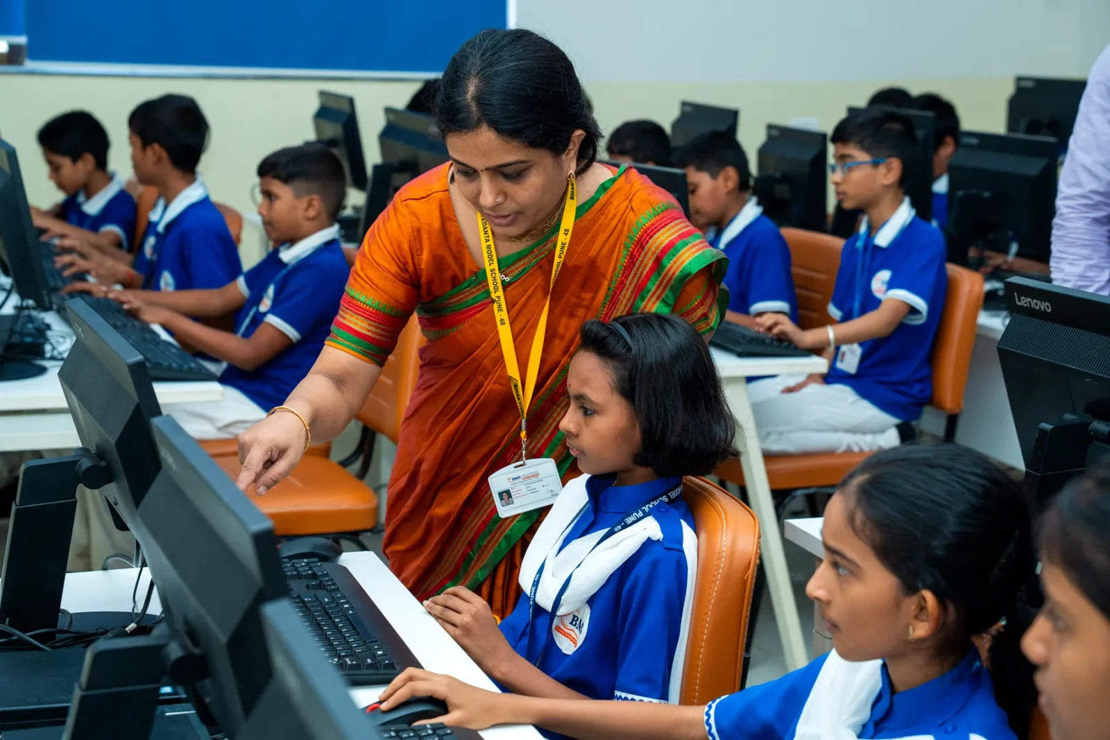A teacher guiding students at the computers in the ICT laboratory