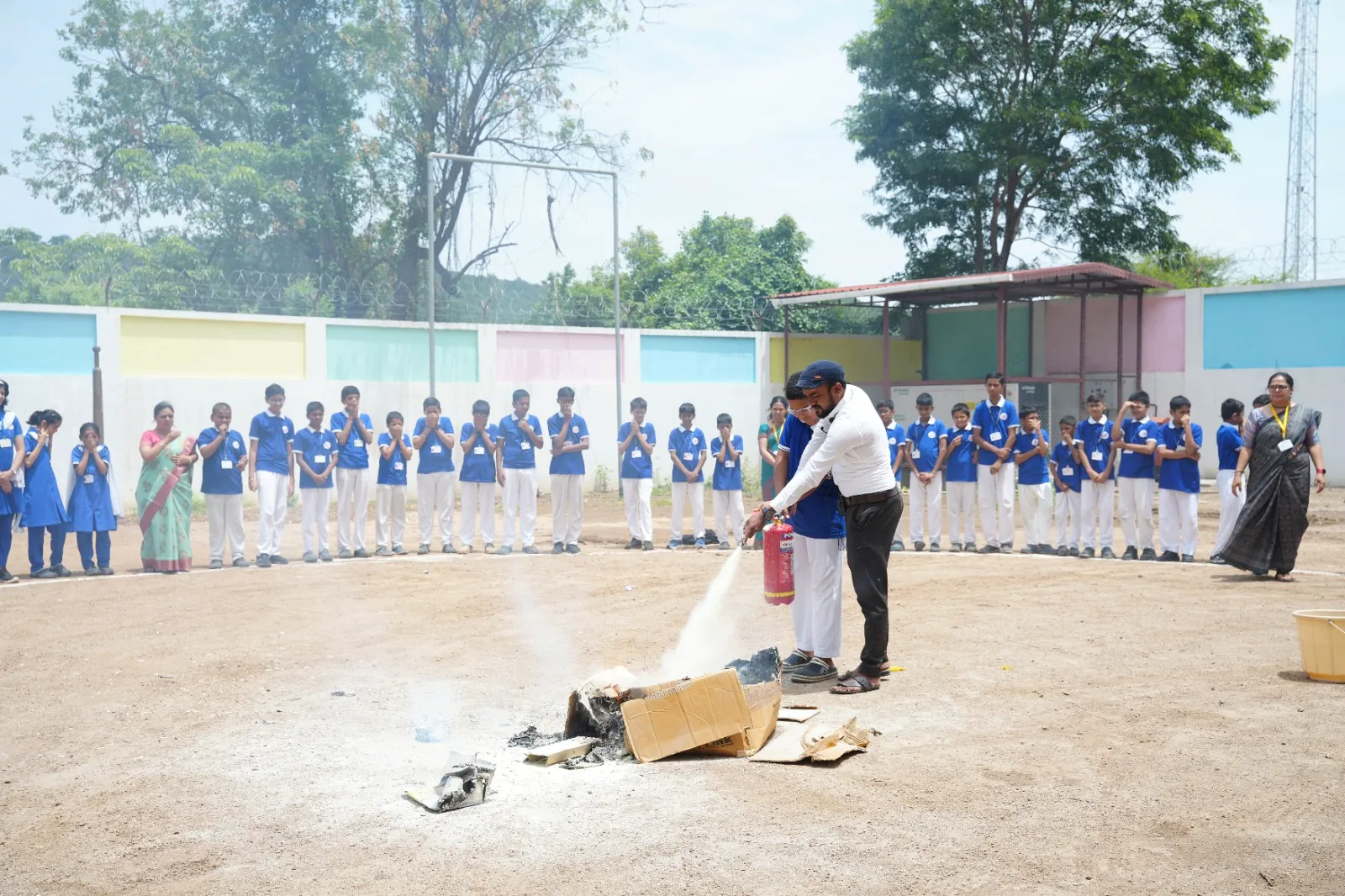 A fire-safety drill on the school ground with a fire extinguisher demonstration