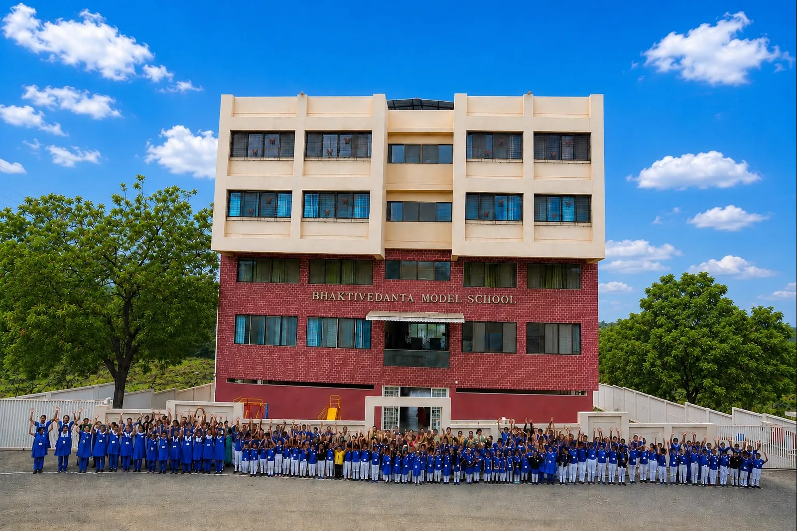 The school building on a clear day, with the whole school assembled in front of it and trees on either side