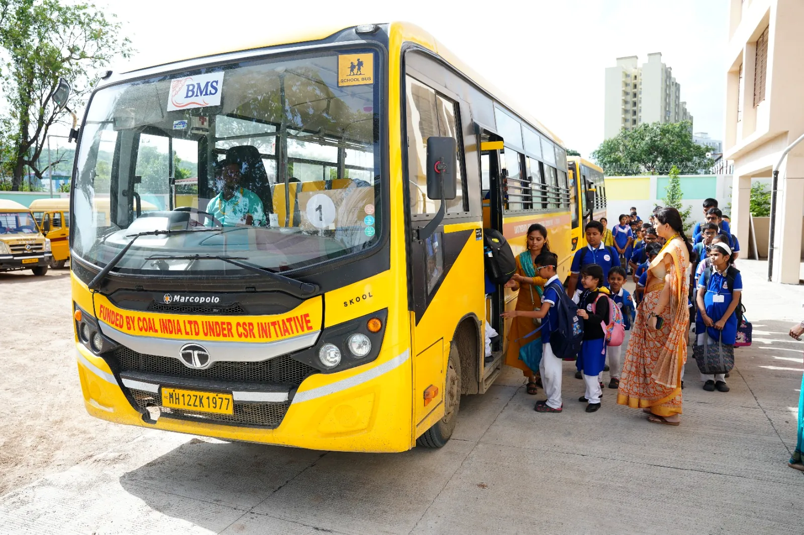 A school bus at the gate with students boarding under staff supervision